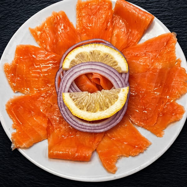Smoked salmon slices arranged on a white plate with red onion rings and lemon wedges.