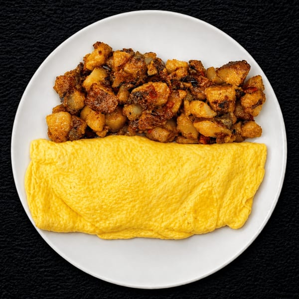A white plate holds a fluffy yellow omelet and a serving of seasoned breakfast potatoes.
