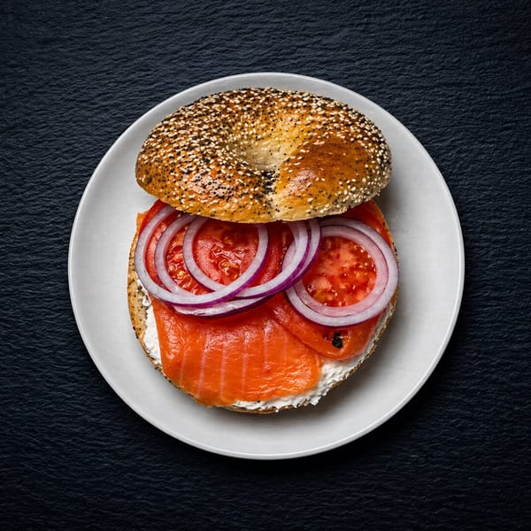 Everything bagel with cream cheese, smoked salmon, tomato, and red onion on a white plate.